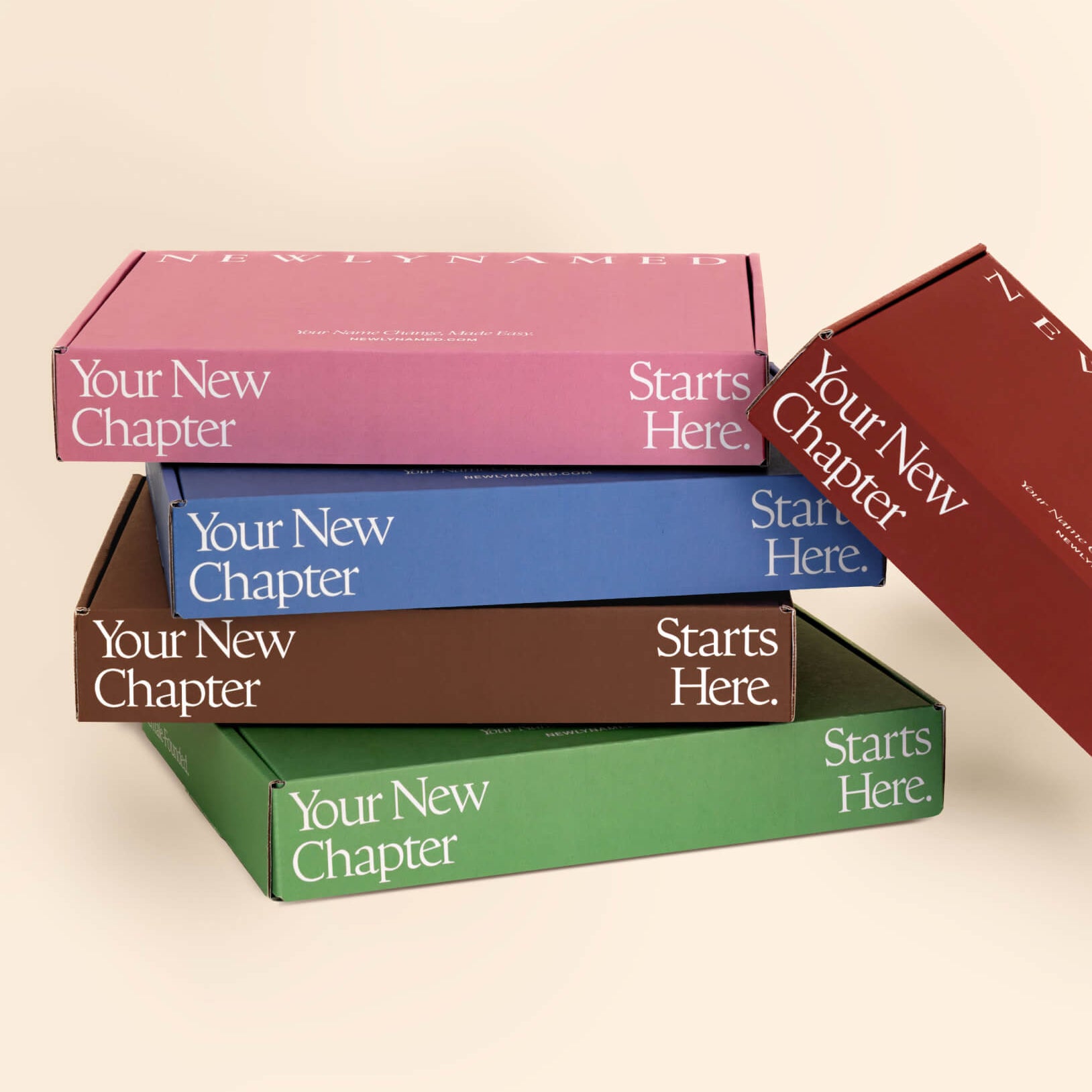 A stack of colorful NewlyNamed name change kit boxes in pink, blue, brown, green, and red with the text Your New Chapter Starts Here.