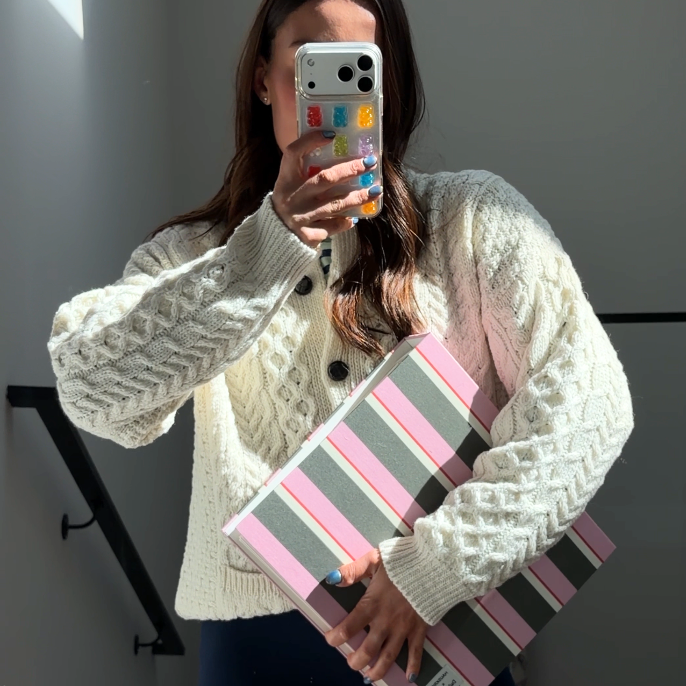 Person holding a striped clutch in front of a mirror