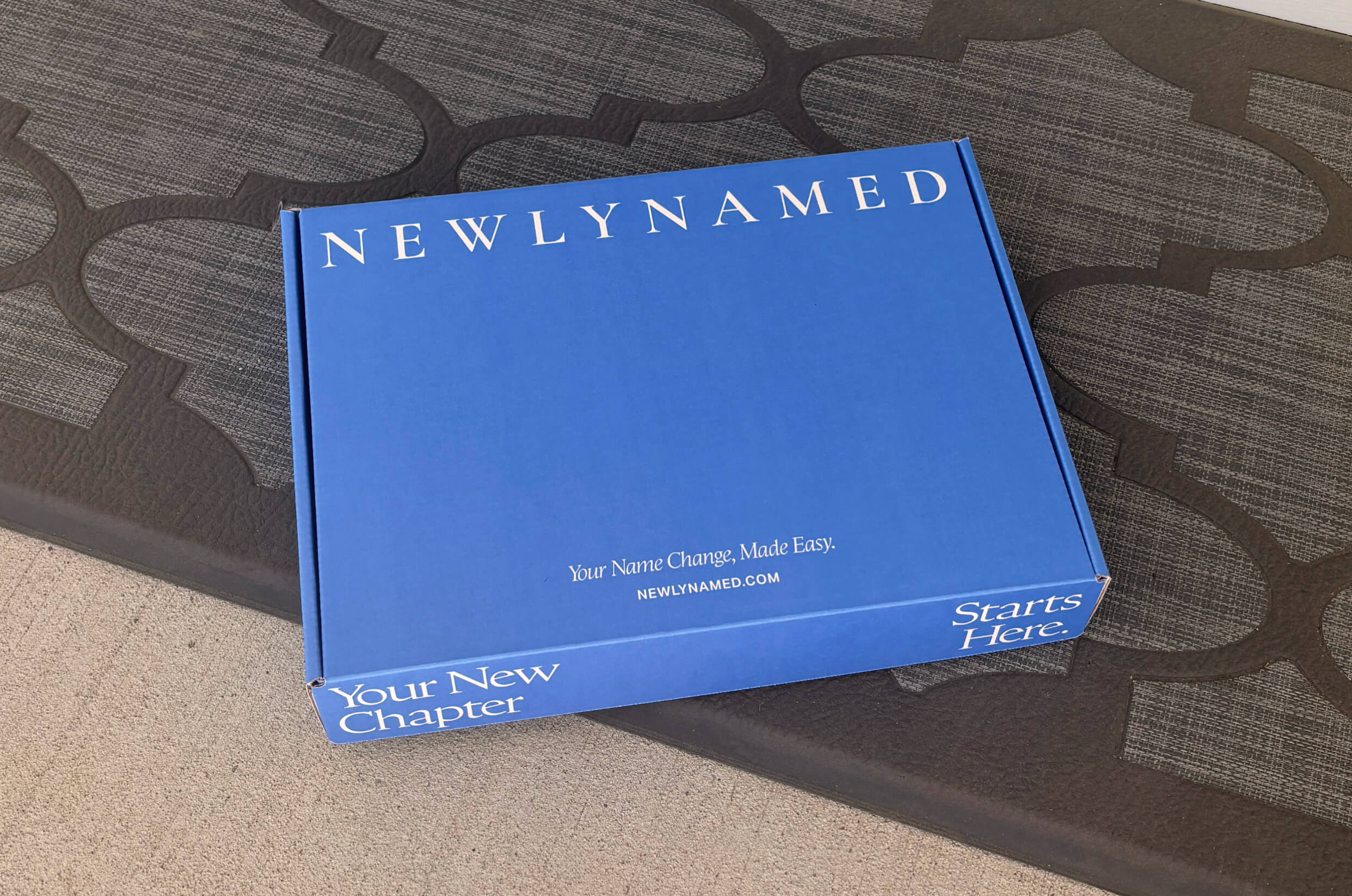 A blue NewlyNamed Box name change kit delivered and sitting on a home doorstep.