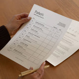 A woman reviewing a printed Parker's Name Change Checklist from a NewlyNamed Print at Home kit next to a marriage certificate.