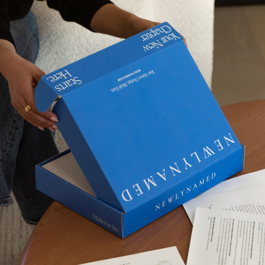 A close-up view of a person’s hands opening a bright blue cardboard box. The top and sides of the box feature white text reading 