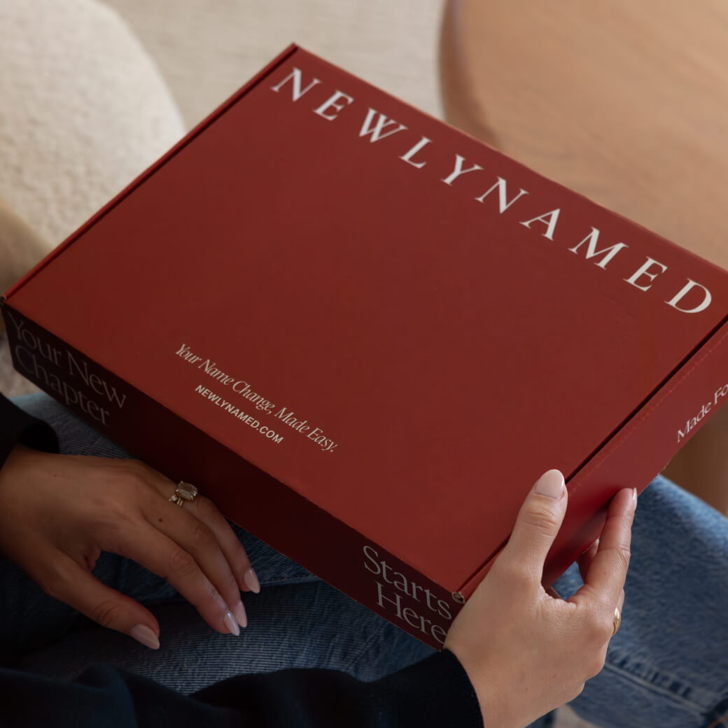 A close-up view of a person wearing jeans holding a closed burgundy red box. The box has 